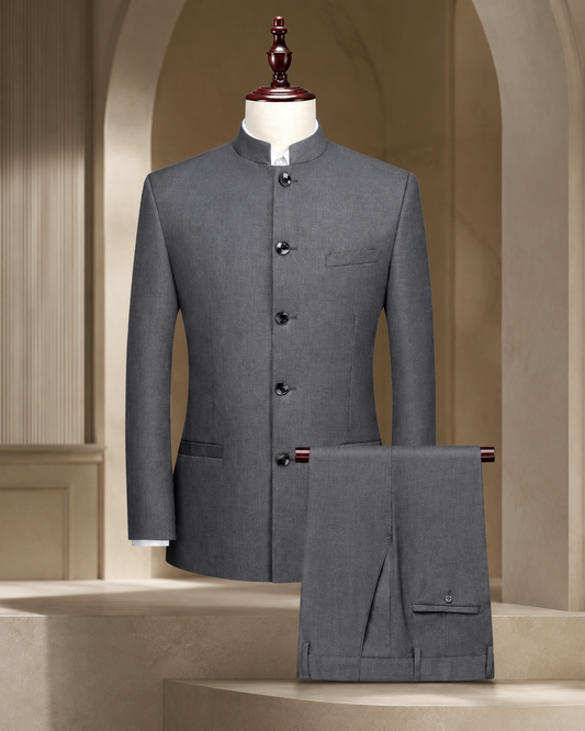 A gray men's traditional suit set consisting of a mandarin-collar jacket displayed on a mannequin and matching trousers draped over a stand, set against a warm beige architectural background.