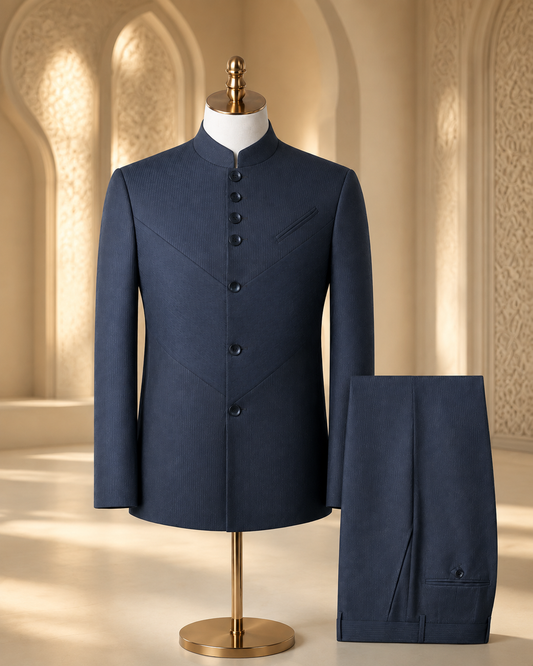 A navy blue traditional suit set consisting of a mandarin-collar jacket displayed on a mannequin and matching trousers folded beside it, set against a warm, ornate architectural background.