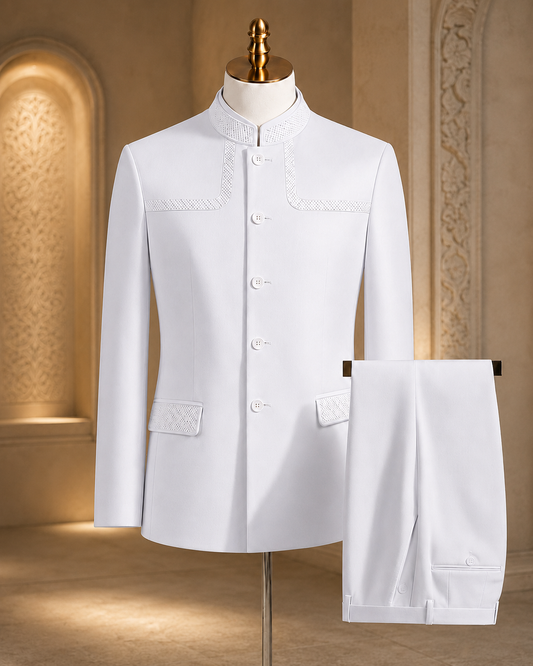 A white traditional men's suit set displayed on a mannequin, featuring a mandarin-collar jacket with decorative embroidery and matching trousers, set against a warm, ornate interior backdrop.